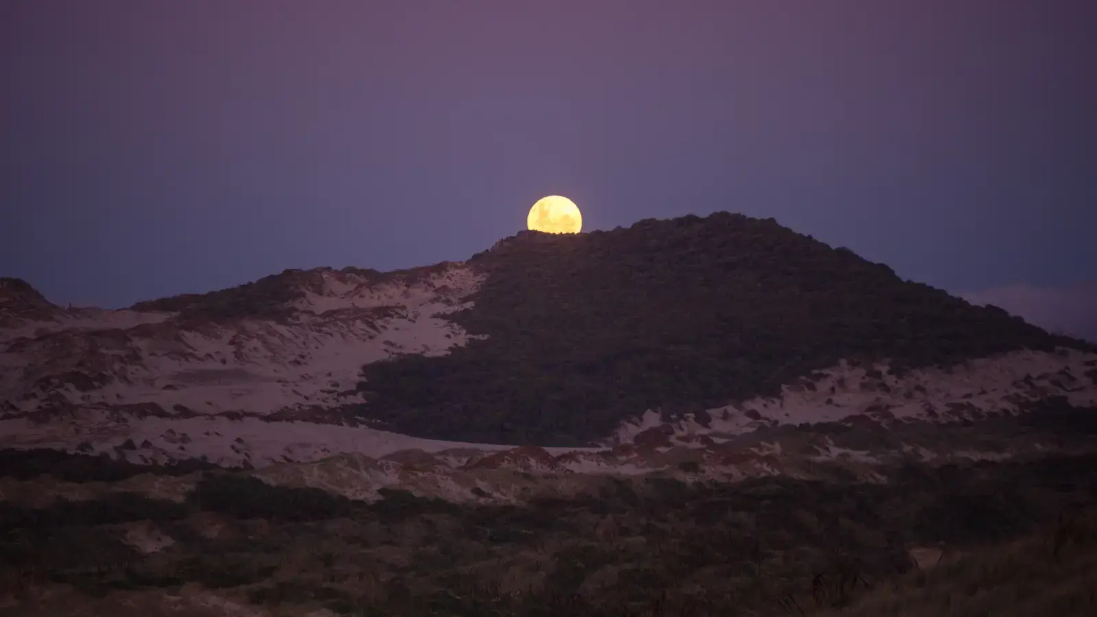 Full moon rising above a rugged, snow-dusted mountain ridge.