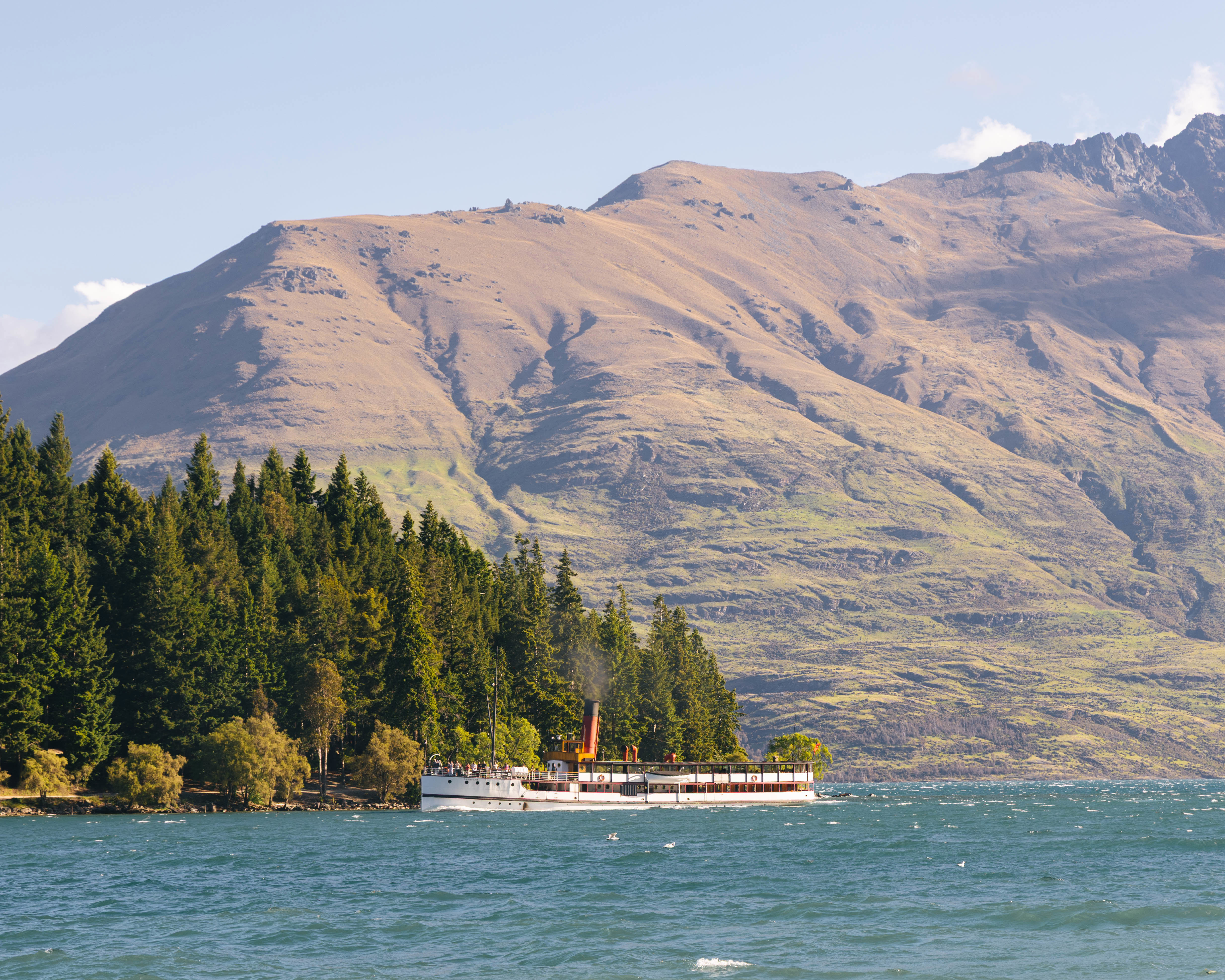The historic TSS Earnslaw vintage steamship cruises past Queenstown Gardens with Cecil Peak mountain in the background.