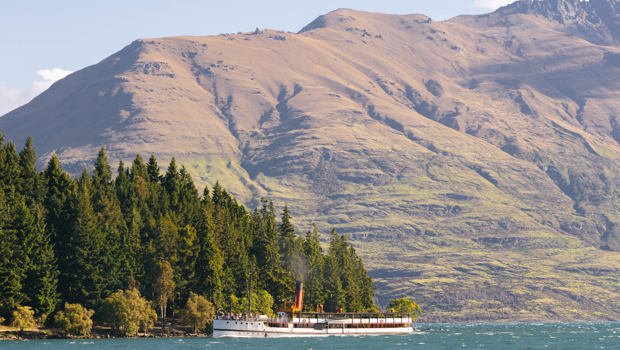The historic TSS Earnslaw vintage steamship cruises past Queenstown Gardens with Cecil Peak mountain in the background.