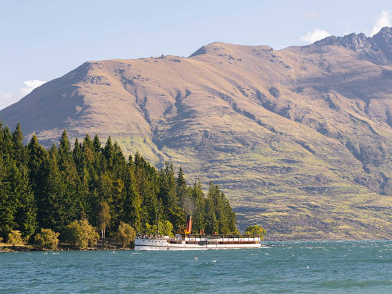 The historic TSS Earnslaw vintage steamship cruises past Queenstown Gardens with Cecil Peak mountain in the background.