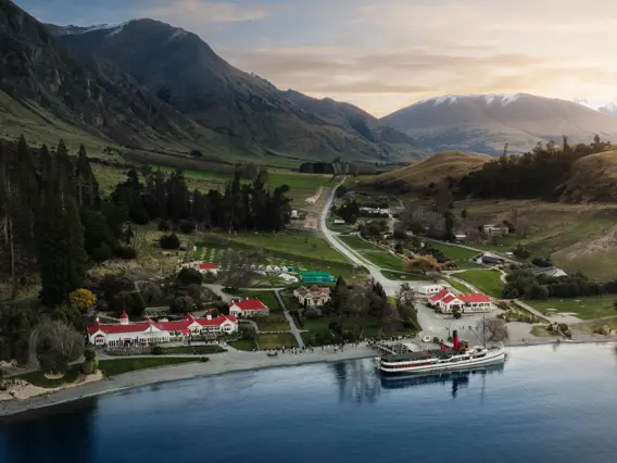 Aerial drone shot of the lakeside Walter Peak High Country Farm with the historic TSS Earnslaw steamship docked at the wharf. 