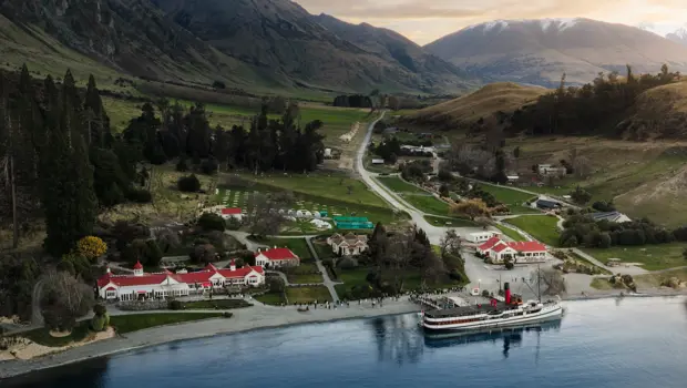 Aerial drone shot of the lakeside Walter Peak High Country Farm with the historic TSS Earnslaw steamship docked at the wharf. 
