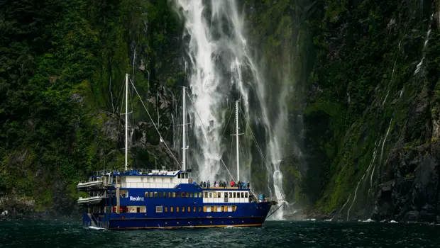 Cruise vessel beneath a towering waterfall in Milford Sound.