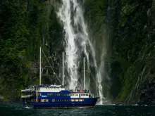 Cruise vessel beneath a towering waterfall in Milford Sound.