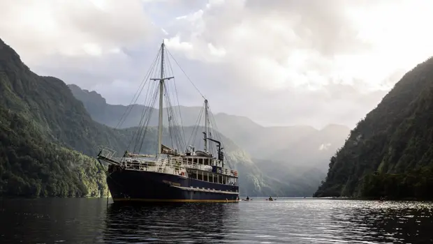Expedition vessel cruising through a dramatic mountain fiord.