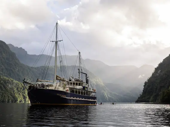 Expedition vessel cruising through a dramatic mountain fiord.