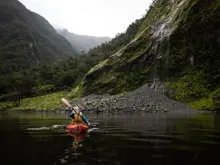 Guest kayaking beneath steep mountains in Dusky Sound.