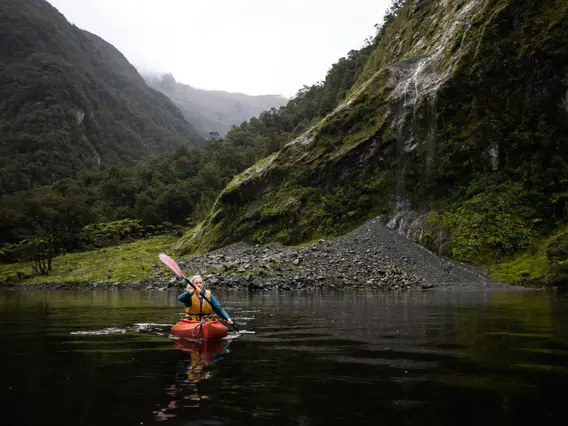 Guest kayaking beneath steep mountains in Dusky Sound.