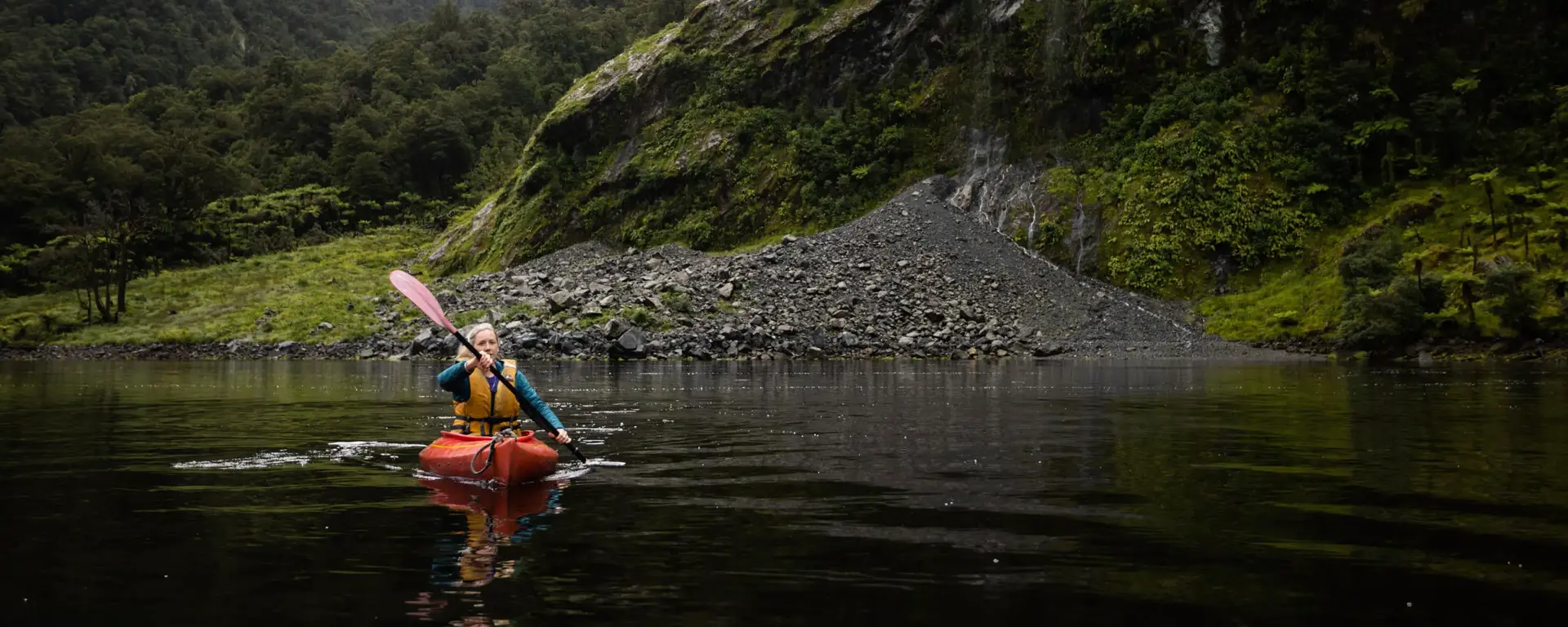 Guest kayaking beneath steep mountains in Dusky Sound.