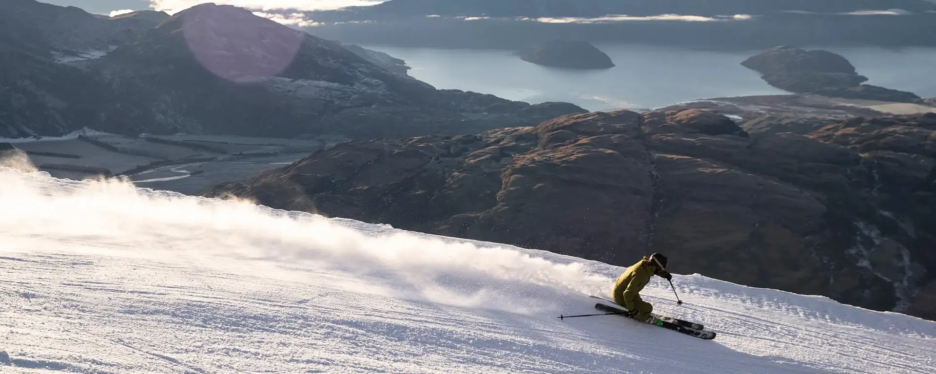 Skier carving down Treble Cone with mountain and lake views.