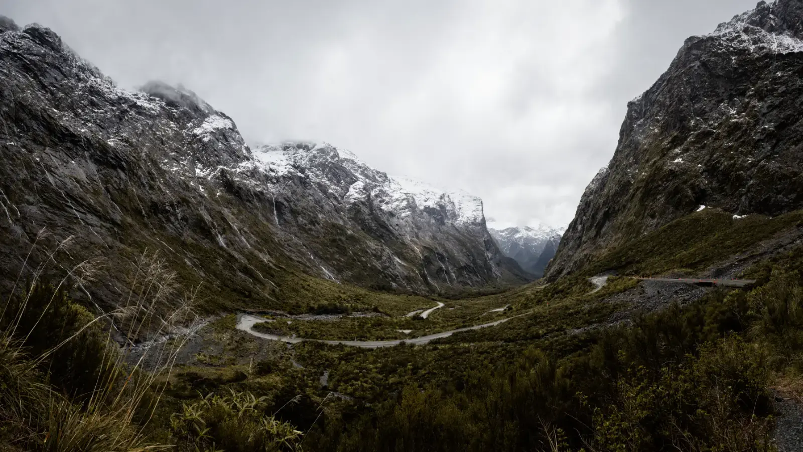 A winding road snaking through a narrow glacial valley flanked by steep, snow-streaked mountain walls