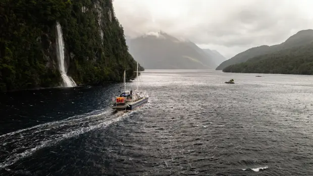 Expedition vessel cruising past a waterfall in Dusky Sound.