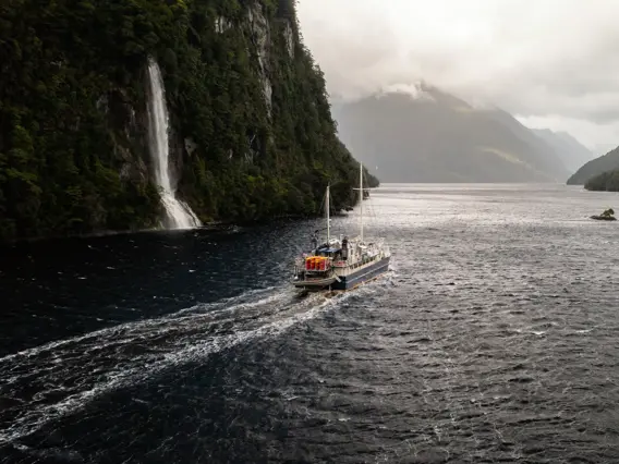 Expedition vessel cruising past a waterfall in Dusky Sound.