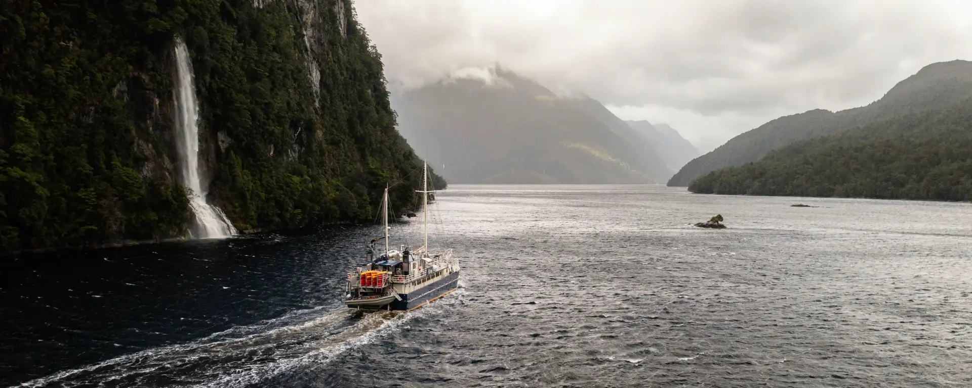 Expedition vessel cruising past a waterfall in Dusky Sound.