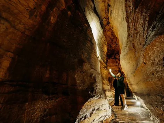 Visitor walking through a narrow rock passage inside the Te Anau Glowworm Caves.