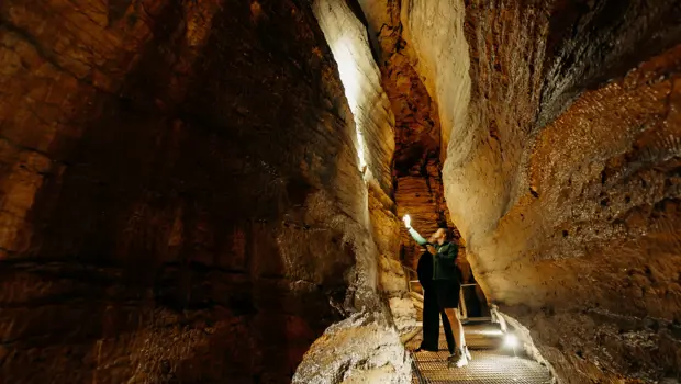 Visitor walking through a narrow rock passage inside the Te Anau Glowworm Caves.
