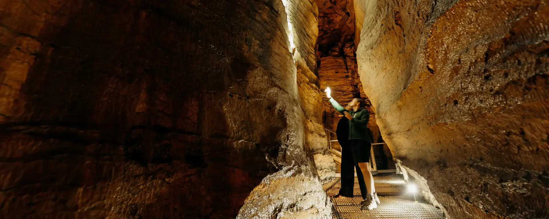 Visitor walking through a narrow rock passage inside the Te Anau Glowworm Caves.