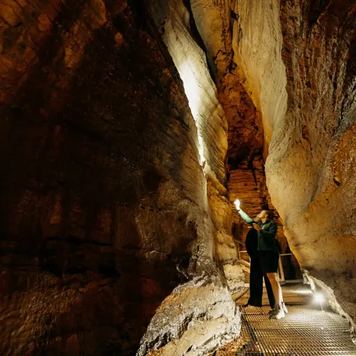 Visitor walking through a narrow rock passage inside the Te Anau Glowworm Caves.