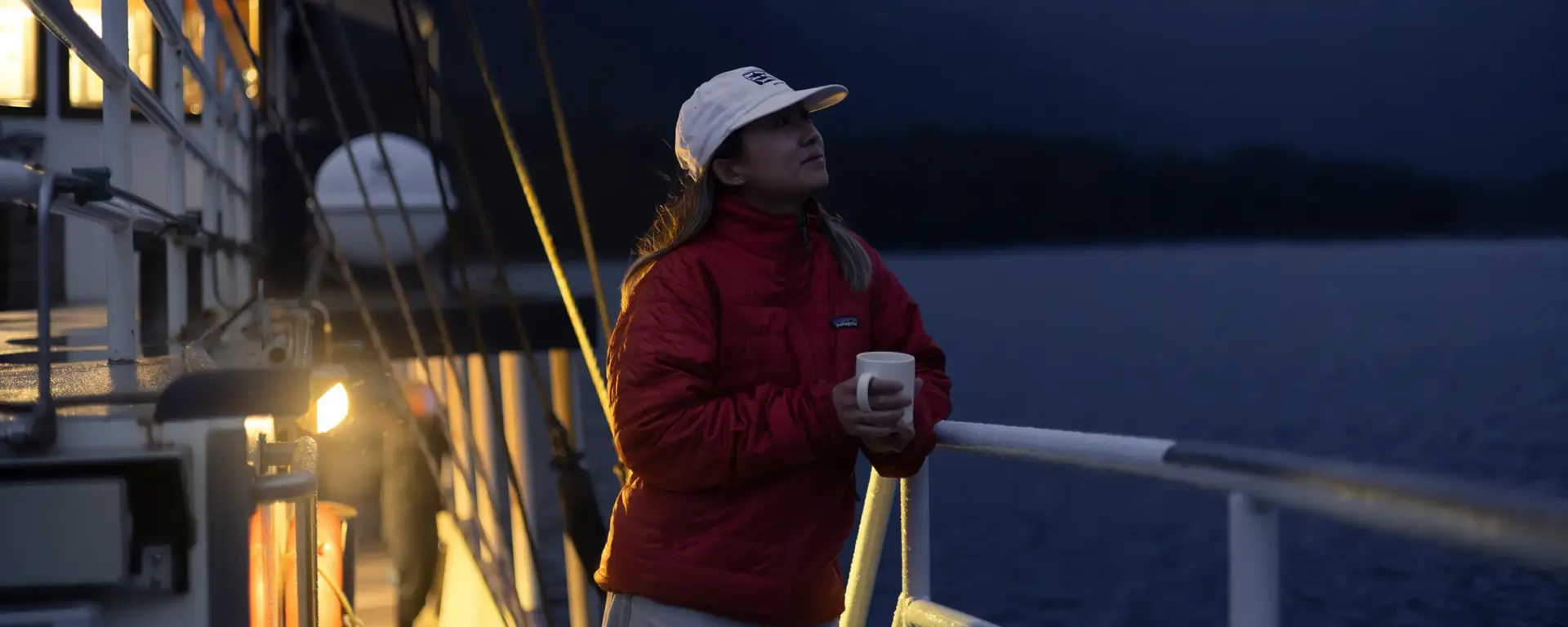 Woman holding a warm drink on a boat during an overnight cruise.