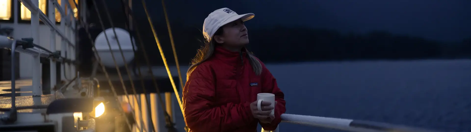 Woman holding a warm drink on a boat during an overnight cruise.