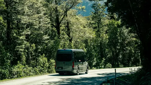 Coach travelling along a road through lush mountain forest.