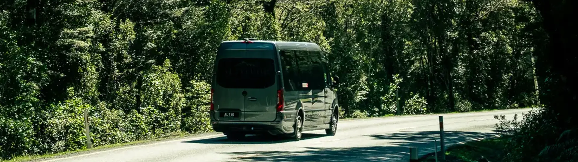 Coach travelling along a road through lush mountain forest.