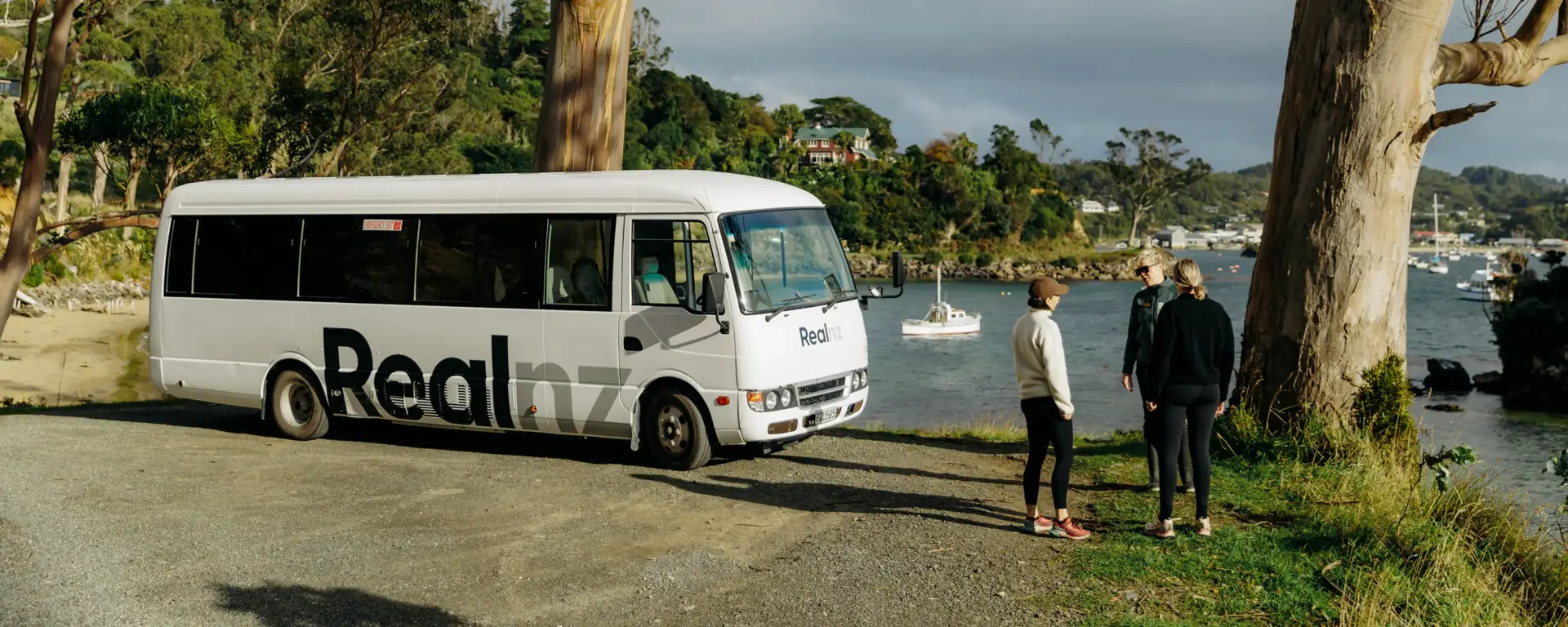 RealNZ coach parked at a scenic coastal viewpoint.