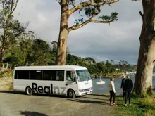 RealNZ coach parked at a scenic coastal viewpoint.
