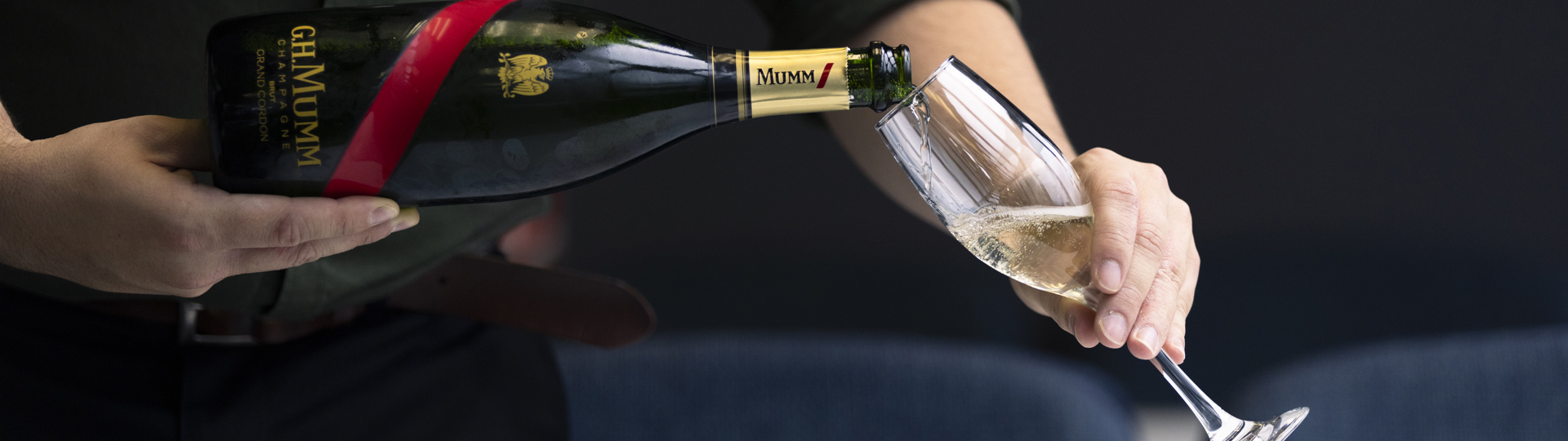 A server in RealNZ branded shirt pours a glass of Mumm champaign. 