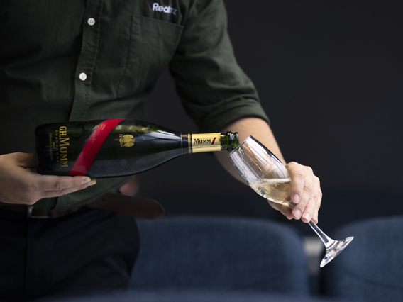 A server in RealNZ branded shirt pours a glass of Mumm champaign. 