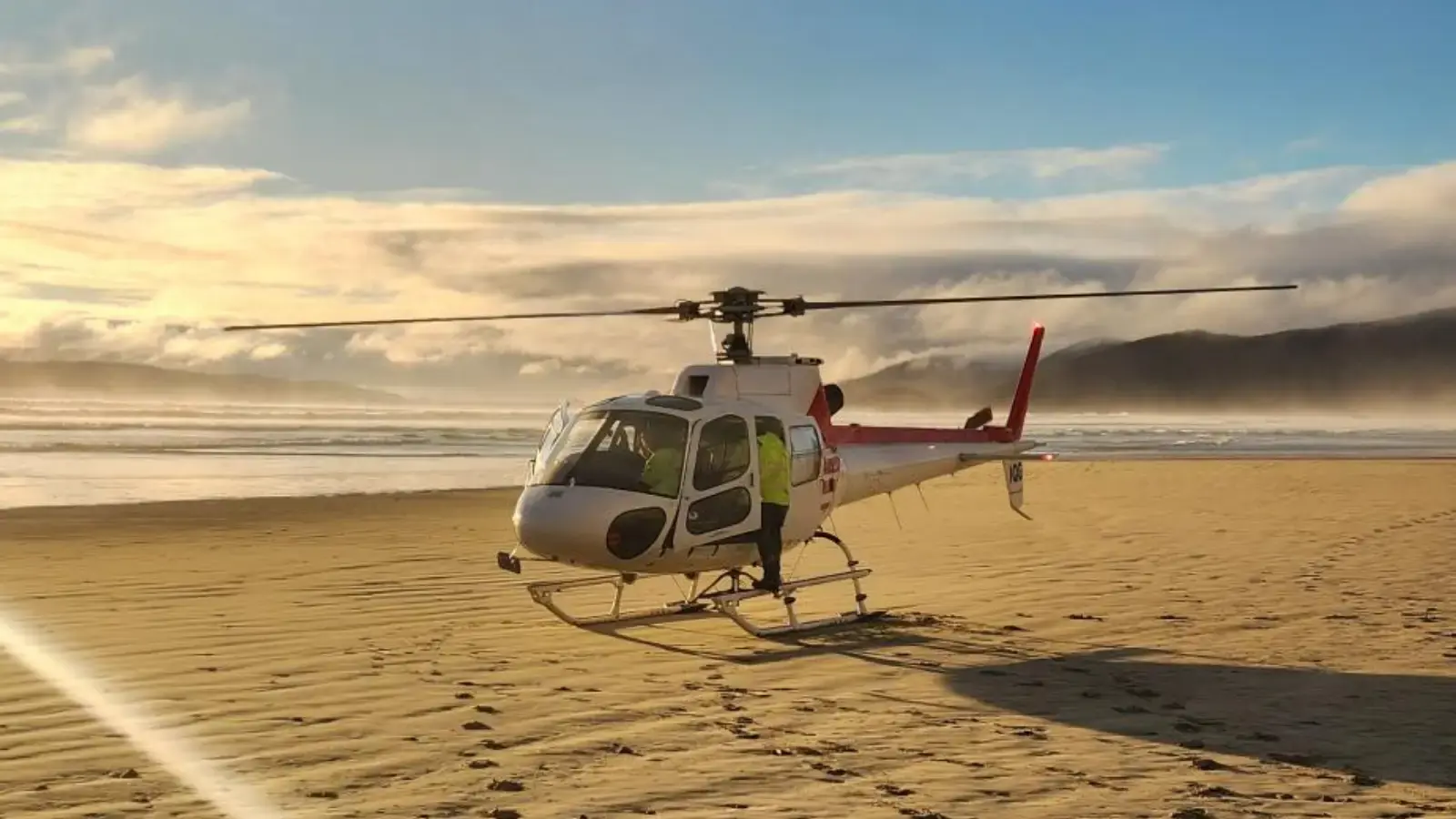A helicopter lands on a sandy beach at golden hour.