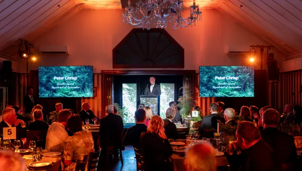 Peter Chrisp, Director General of Department of Conservation, makes a speech on a stage to a room full of people dressed in black tie.