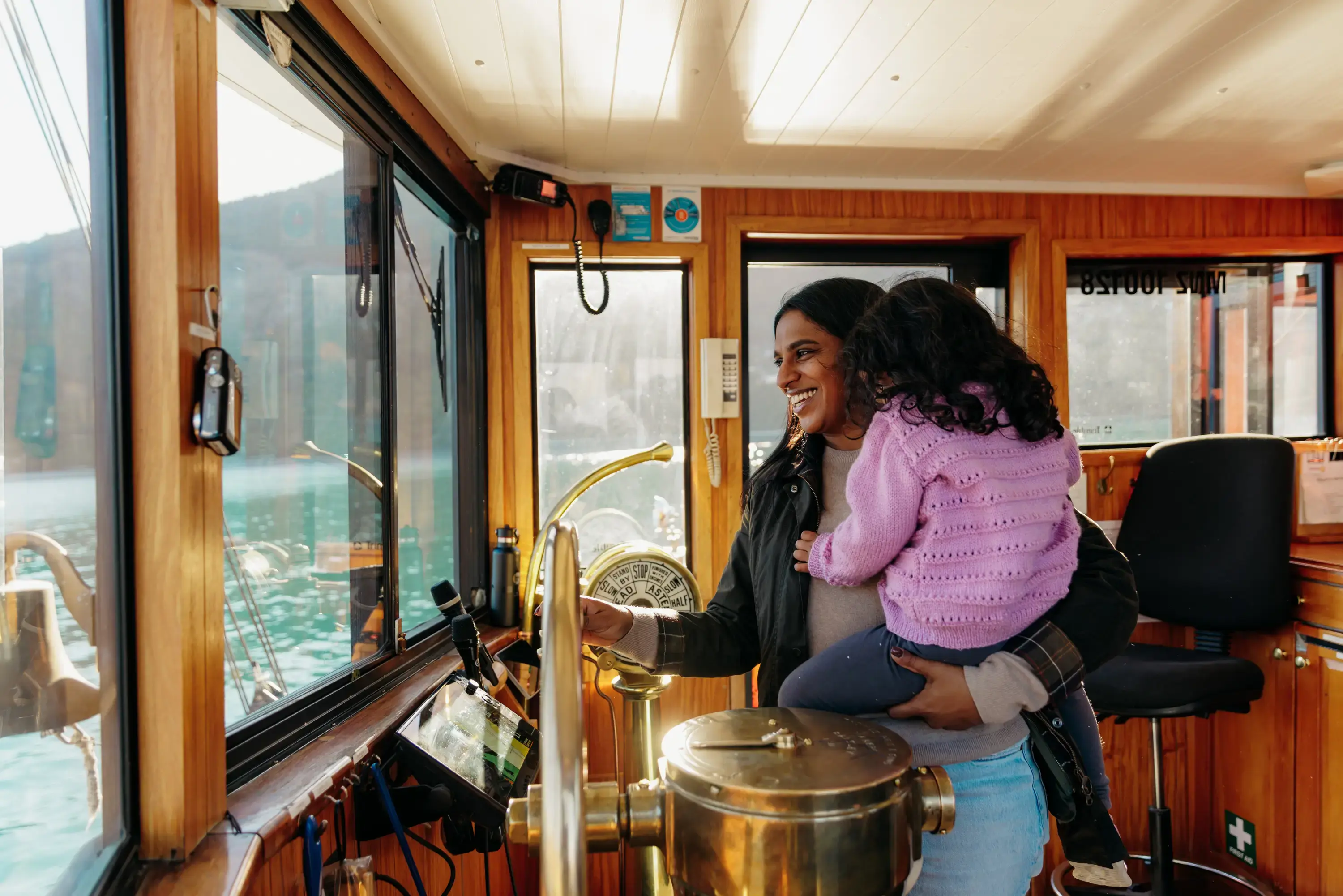 Adult holding a child inside the wheelhouse of a boat on Lake Whakatipu.