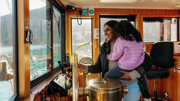 Adult holding a child inside the wheelhouse of a boat on Lake Whakatipu.