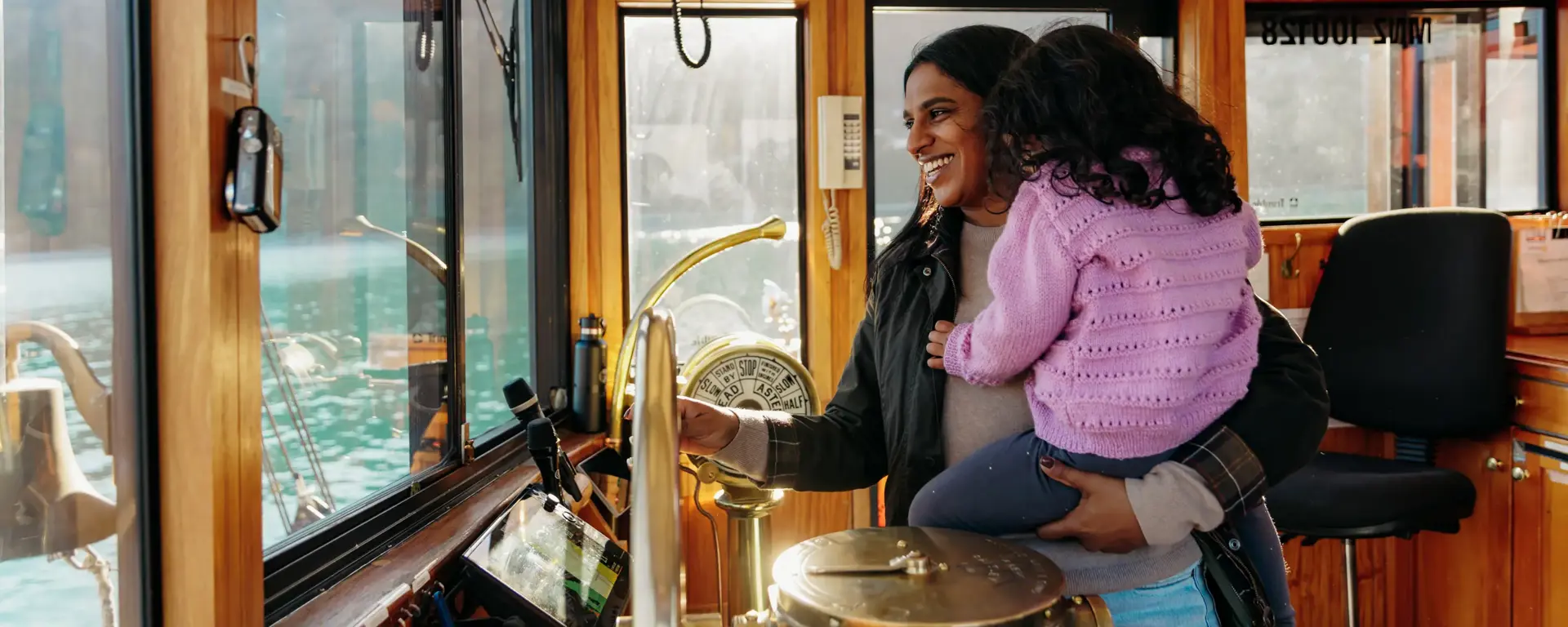 Adult holding a child inside the wheelhouse of a boat on Lake Whakatipu.