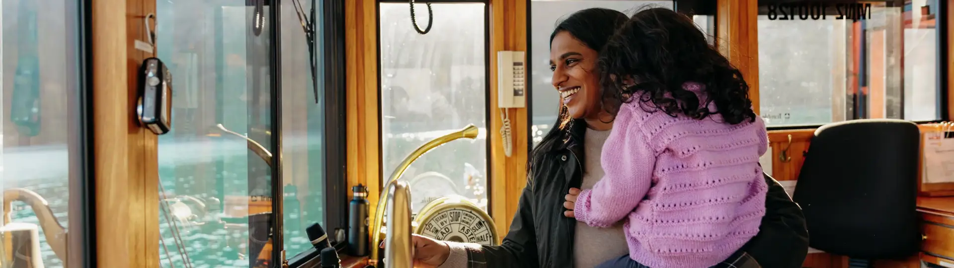 Adult holding a child inside the wheelhouse of a boat on Lake Whakatipu.