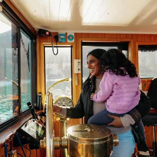 Adult holding a child inside the wheelhouse of a boat on Lake Whakatipu.