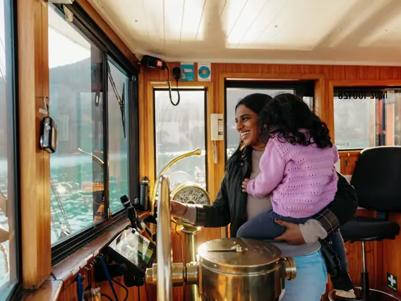 Adult holding a child inside the wheelhouse of a boat on Lake Whakatipu.