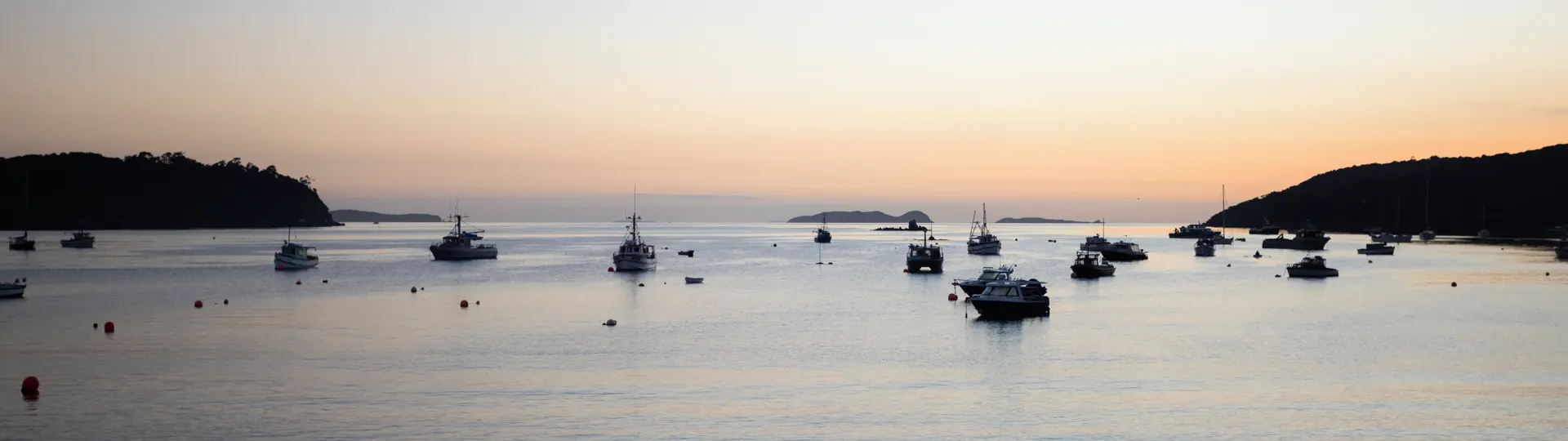 Calm coastal bay at golden hour with sailboats in the distance.