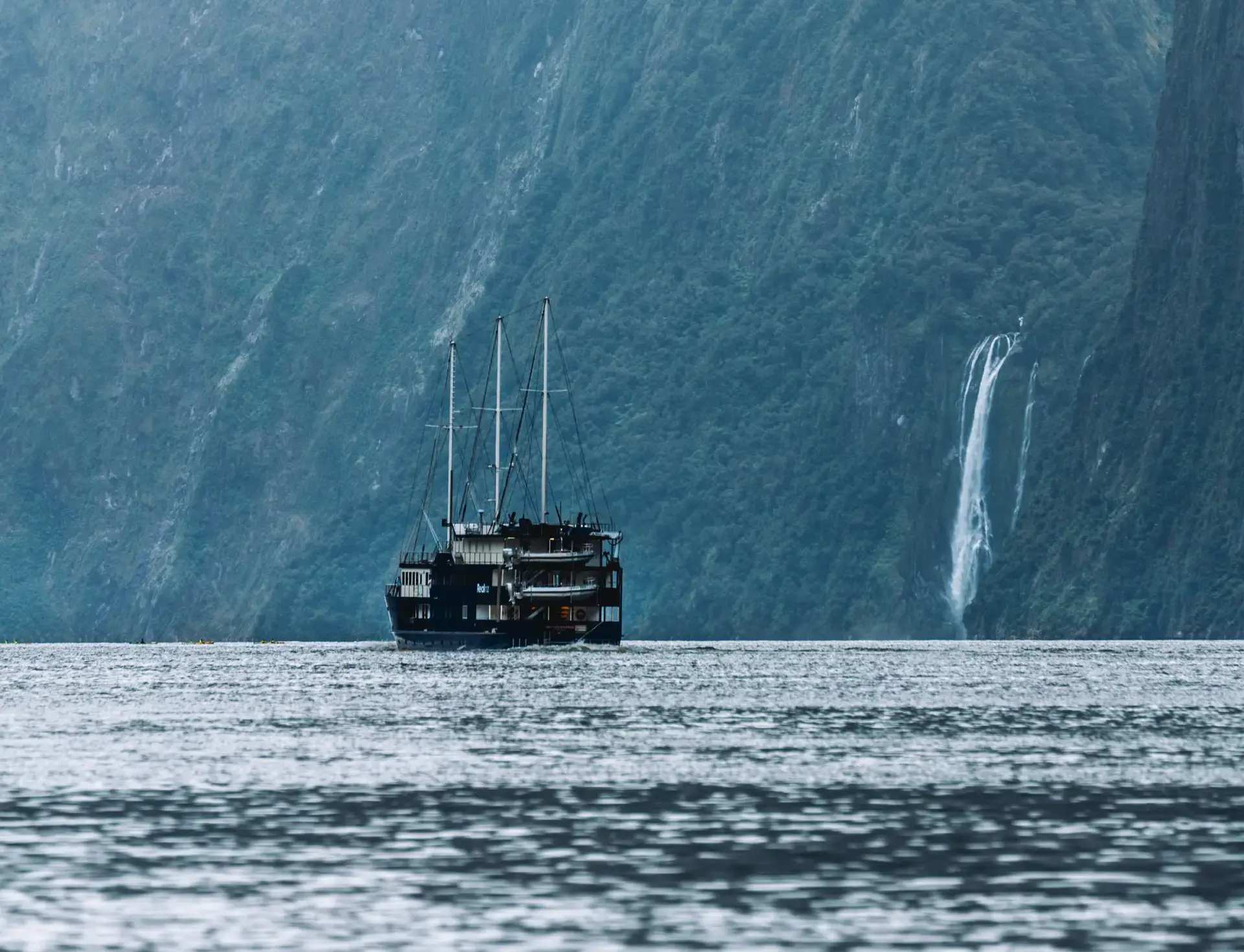 A RealNZ branded tourism overnight boat sails past a waterfall in calm waters in Milford Sound.