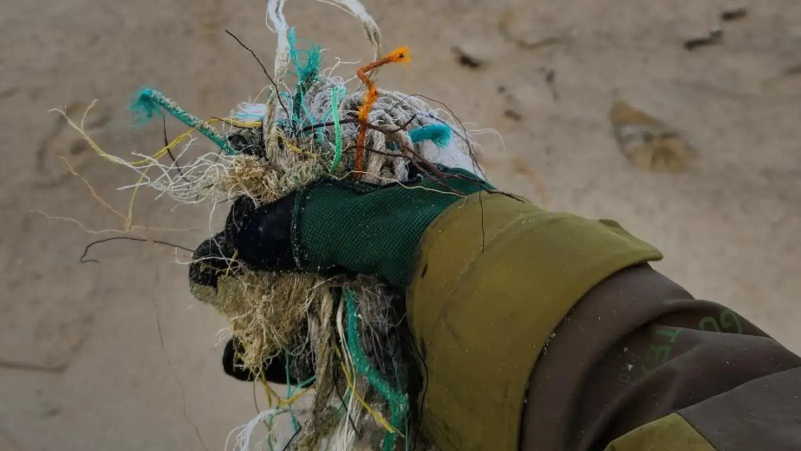 A gloved hand holds a pile of rubbish found in a beach clean up.