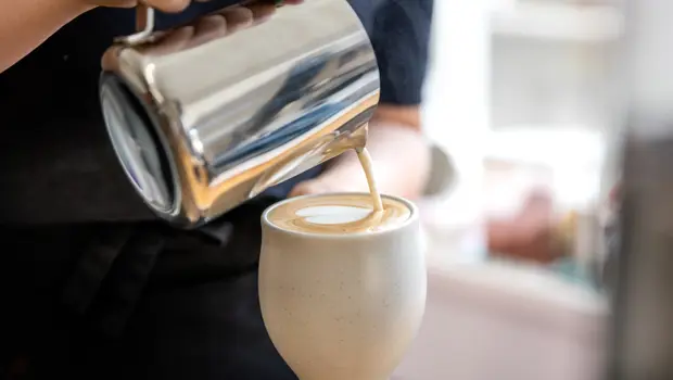 Close up of a barista pouring a flat white with coffe with love heart coffee art into a mug.