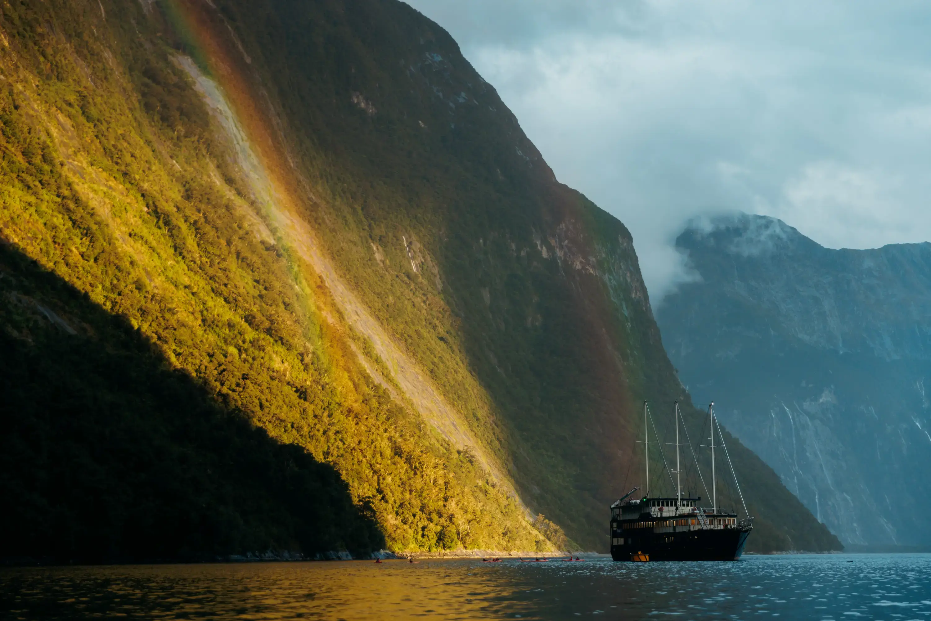 Cruise vessel sailing through dramatic sunlit mountains in Milford Sound.