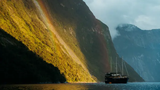 Cruise vessel sailing through dramatic sunlit mountains in Milford Sound.