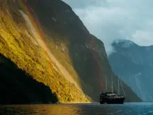 Cruise vessel sailing through dramatic sunlit mountains in Milford Sound.