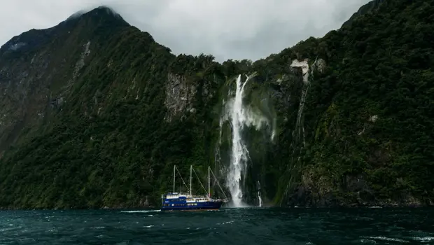 Boat cruising beneath a towering waterfall in Milford Sound.