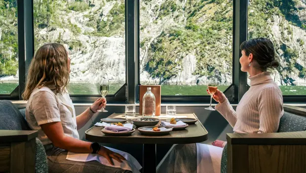 Two guests dining beside large windows overlooking Milford Sound.