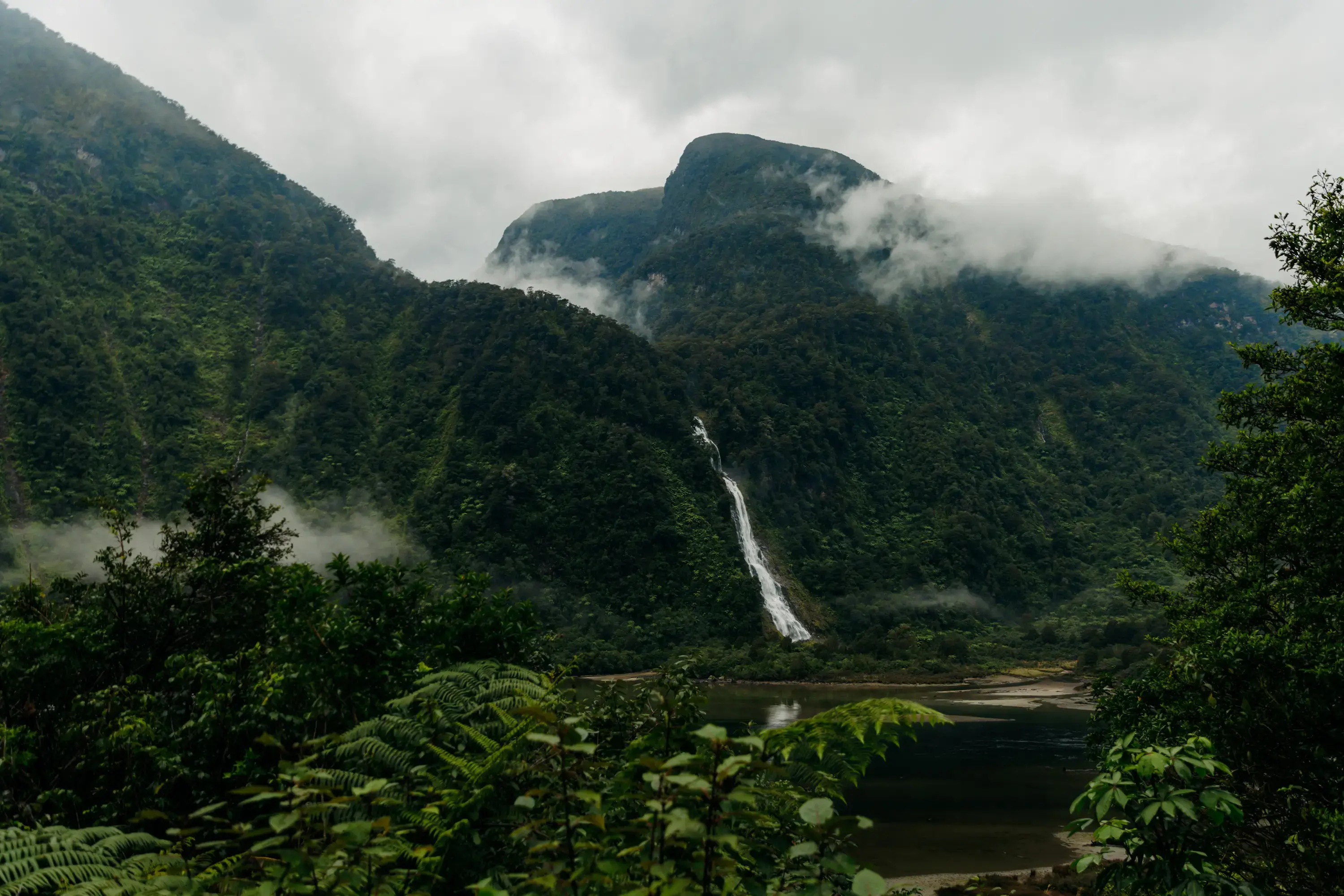 Mist-covered mountains and a waterfall rising above a remote fiord.