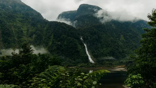 Mist-covered mountains and a waterfall rising above a remote fiord.