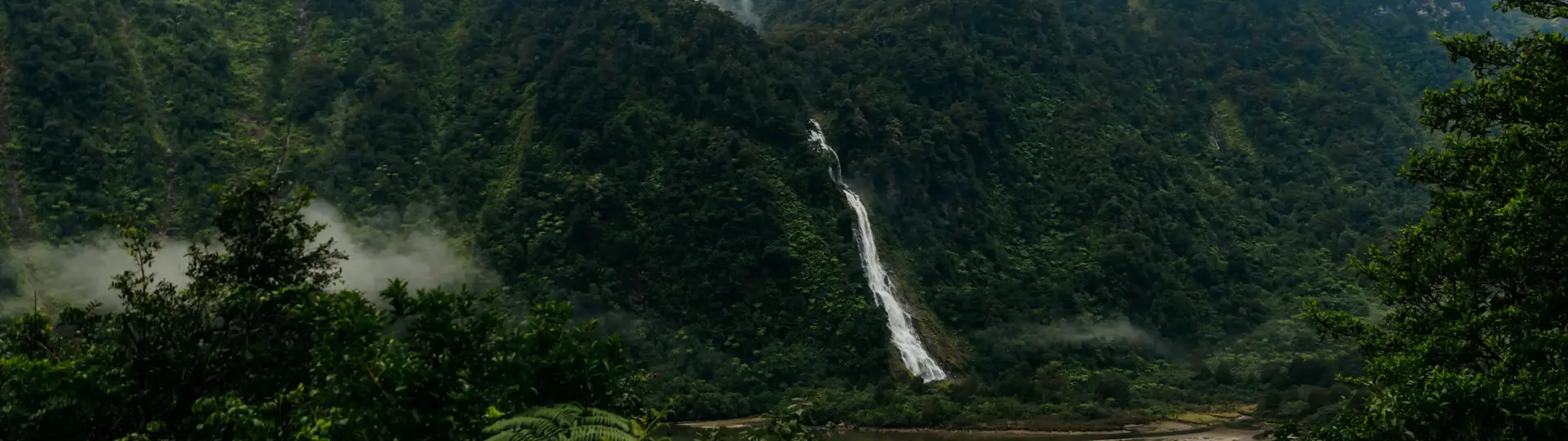 Mist-covered mountains and a waterfall rising above a remote fiord.